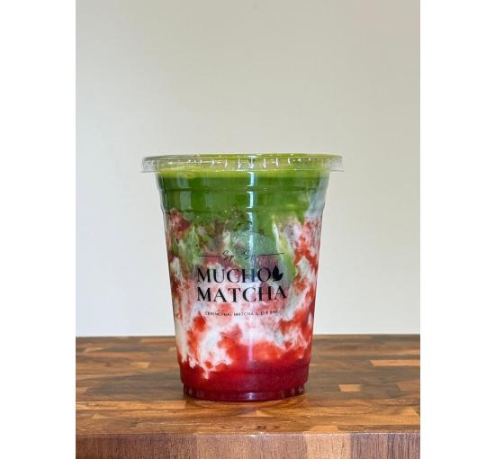 Iced strawberry matcha latte in a Mucho Matcha cup, layered green matcha over strawberry and cream on a wood counter