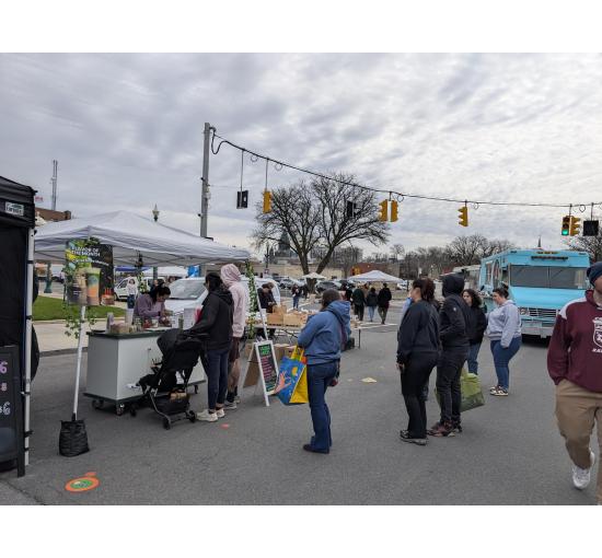 Customers lined up at the Mucho Matcha cart at a Schenectady farmers market, beside an April carrot cake matcha flavor sign