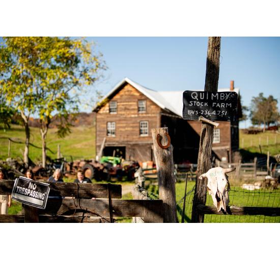 Hand- painted rustic "Quimby Stock Farm" sign. Old wooden barn in the background. 