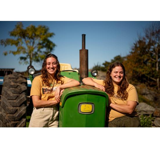 Sisters Emily and Abigail Henry who are the main farmers at Quimby Farm. Posing next to a green tractor.