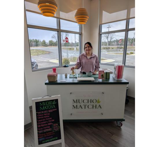 Karina posing at the cart set up for an indoor event, with the menu board in the foreground
