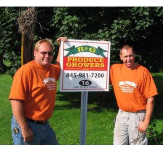 2 men in orange shirts standing by their sign