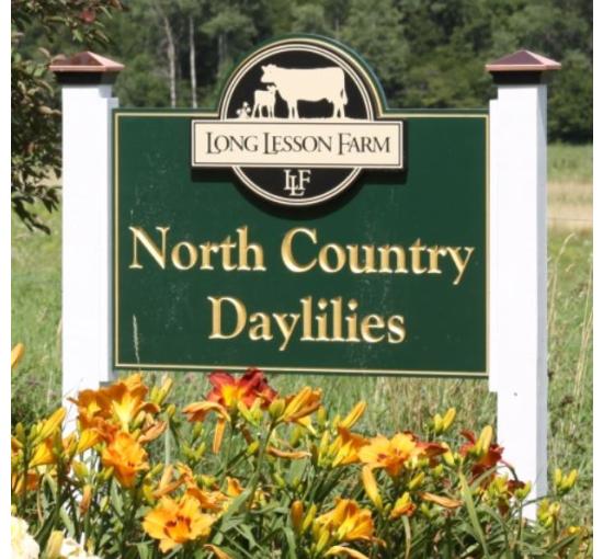 green sign outside of the farm with flowers in front