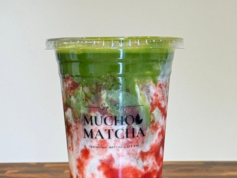 Iced strawberry matcha latte in a Mucho Matcha cup, layered green matcha over strawberry and cream on a wood counter