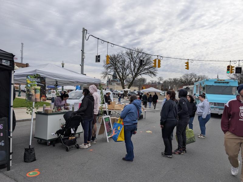 Customers lined up at the Mucho Matcha cart at a Schenectady farmers market, beside an April carrot cake matcha flavor sign