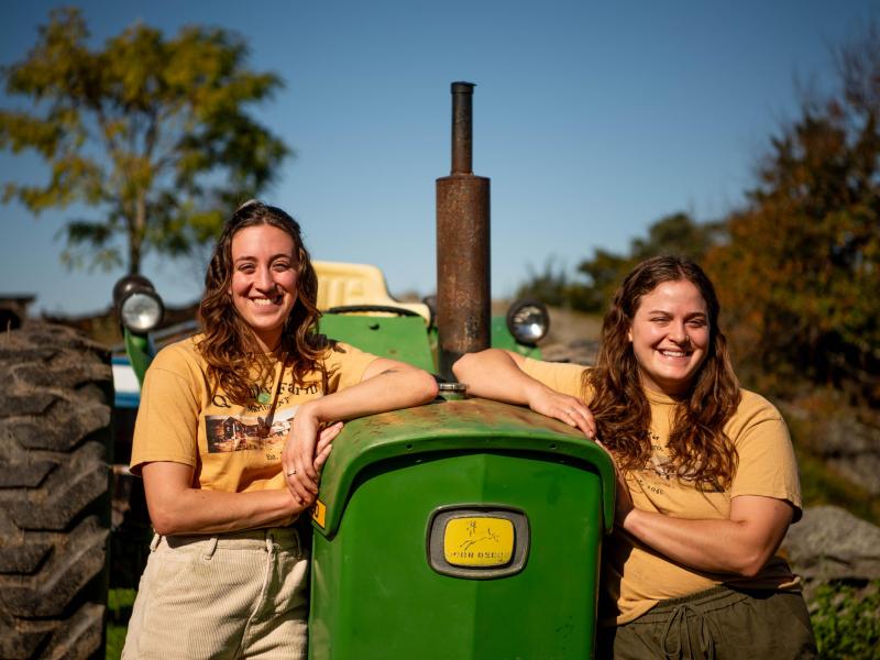 Sisters Emily and Abigail Henry who are the main farmers at Quimby Farm. Posing next to a green tractor.