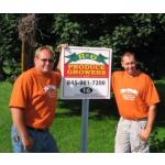 2 men in orange shirts standing by their sign