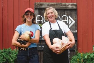 Image of 2 women holding chickens with AOOA logo on the barn in the back