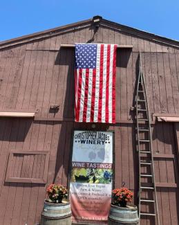 the barn at winery with american flag hanging, logo on the building blue skies and a ladder going up the barn