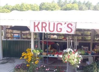 Farm stand with white roof and sign with red font