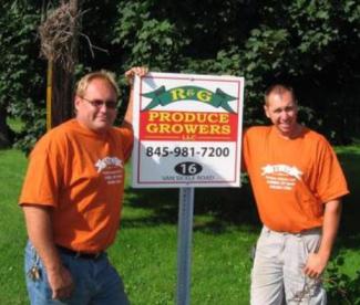 2 men in orange shirts standing by their sign